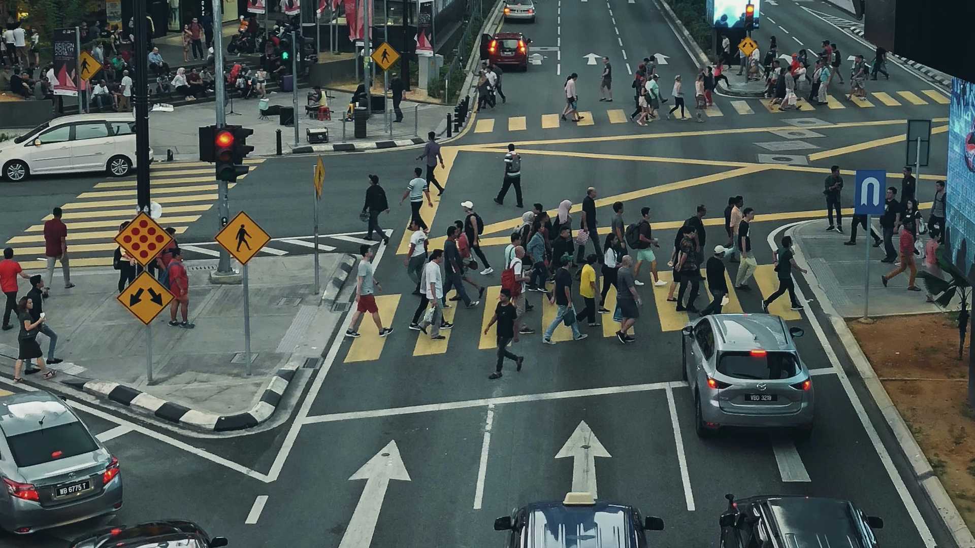 Picture of a busy street with people crossing the road and cars waiting