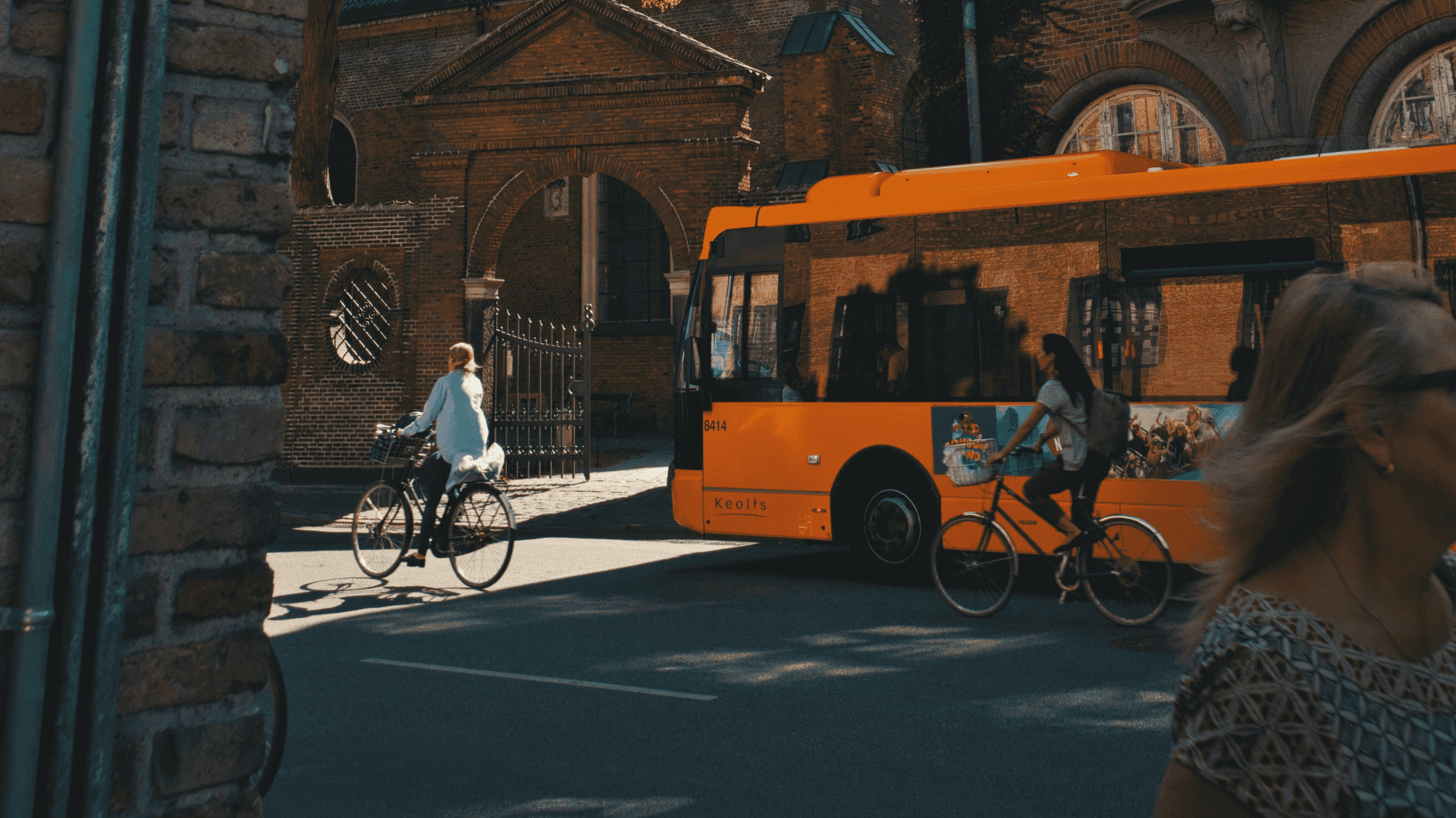 Image of a street view with cyclists on the bike lane, a bus driving on its lane, and a woman walking on the sidewalk.